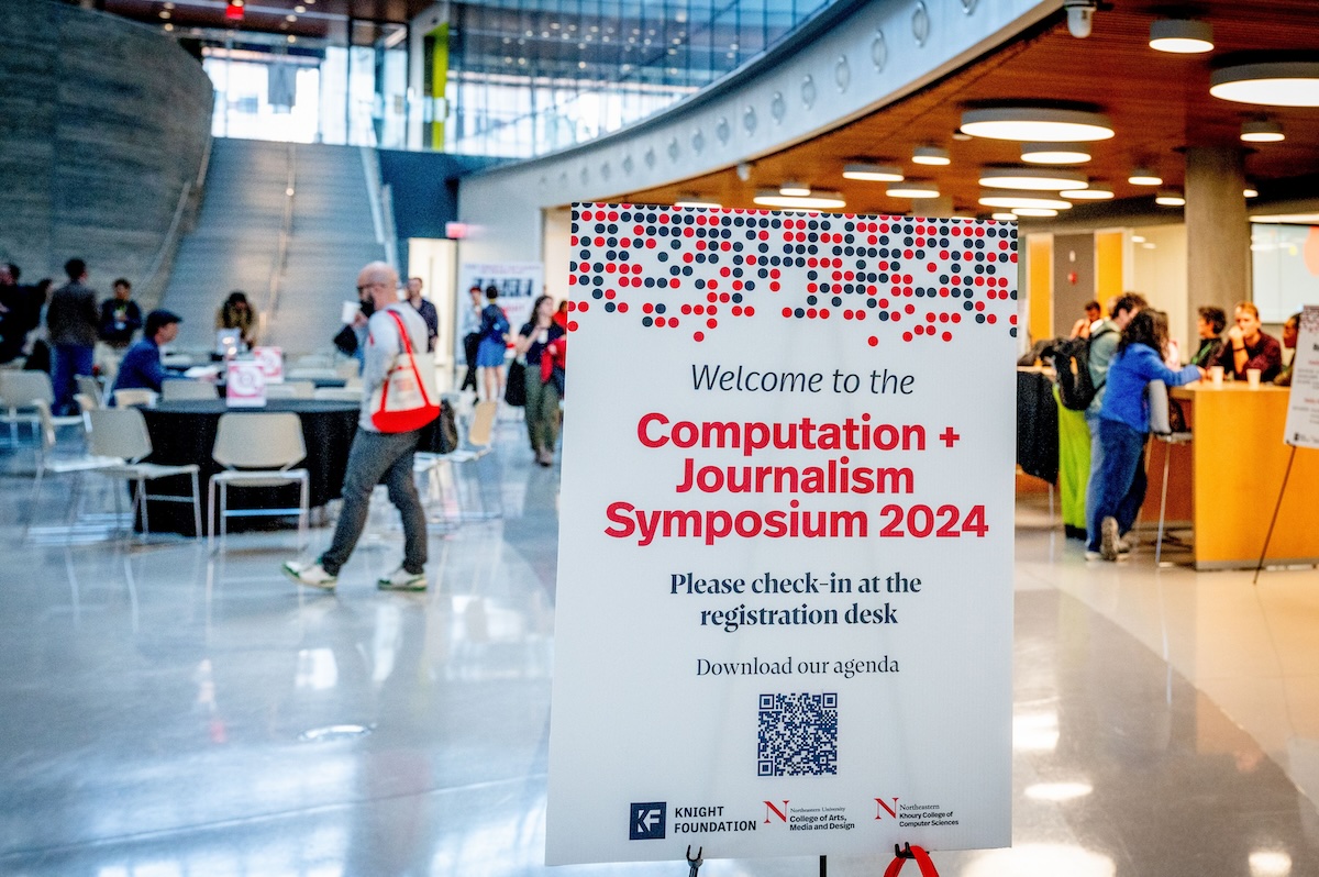 photo from event reception area with sign and blurred people and tables behind