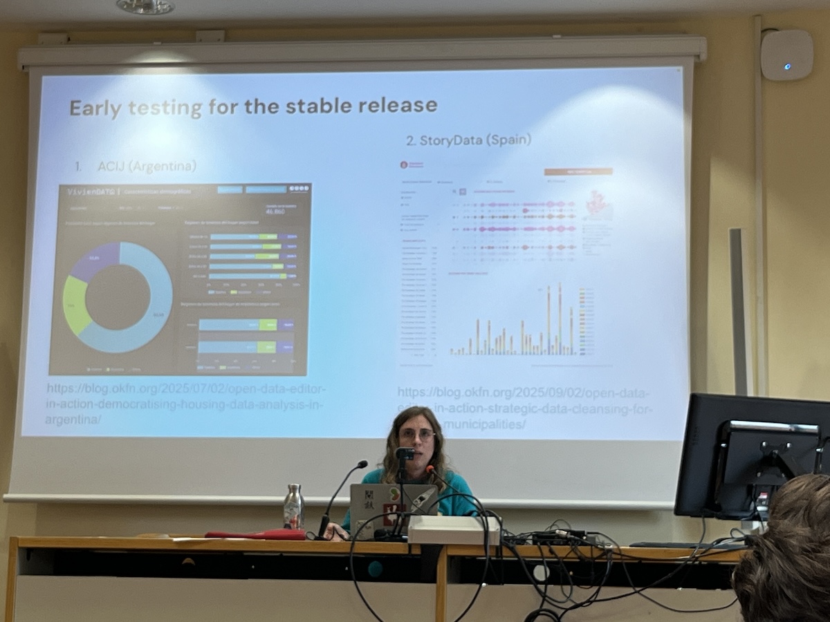 a woman sits behind a desk with a computer and microphone, with two screenshots on a slide behind her