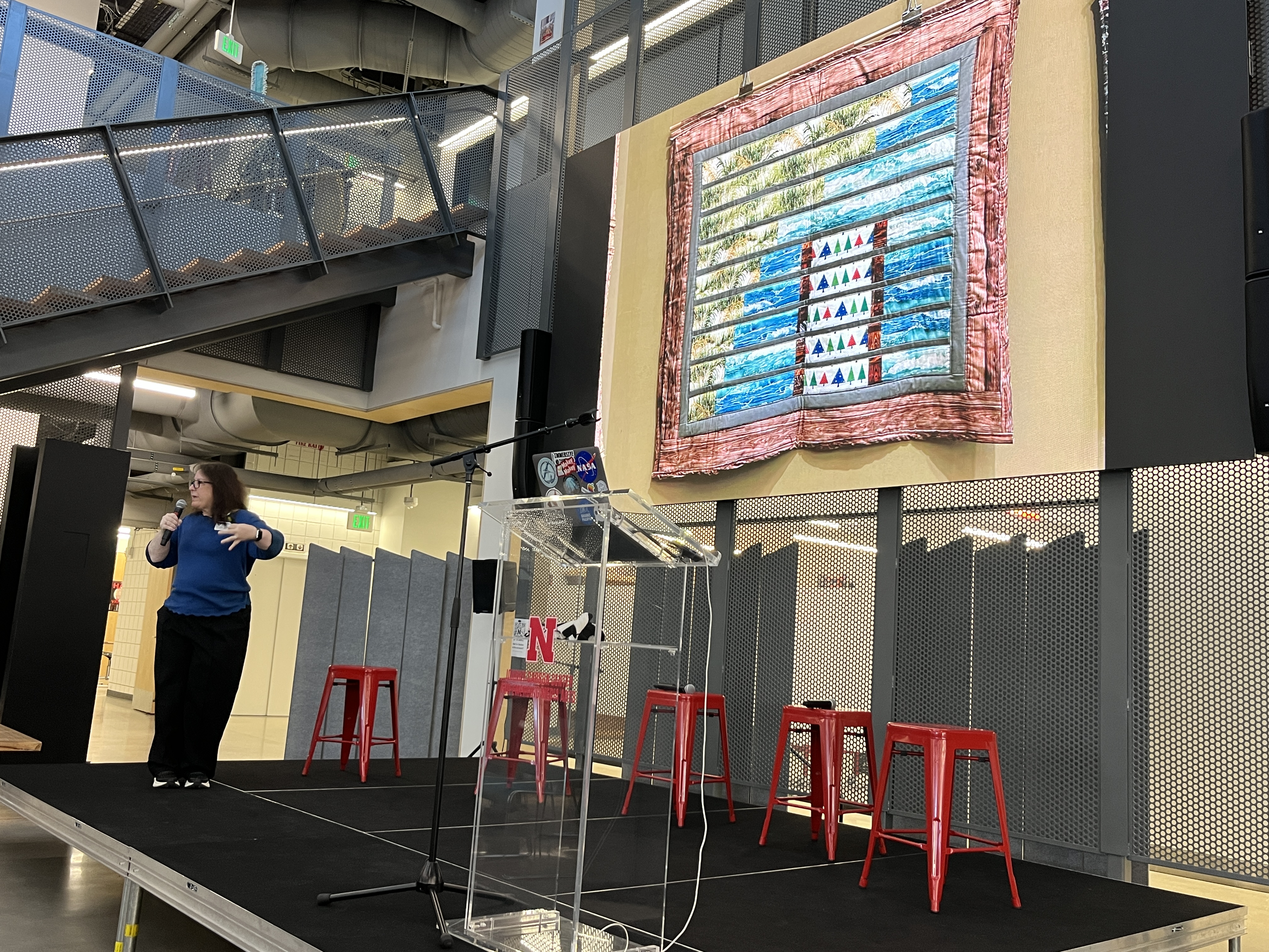 photo of Dr. Guertin speaking on stage with slide behind showing a quilt