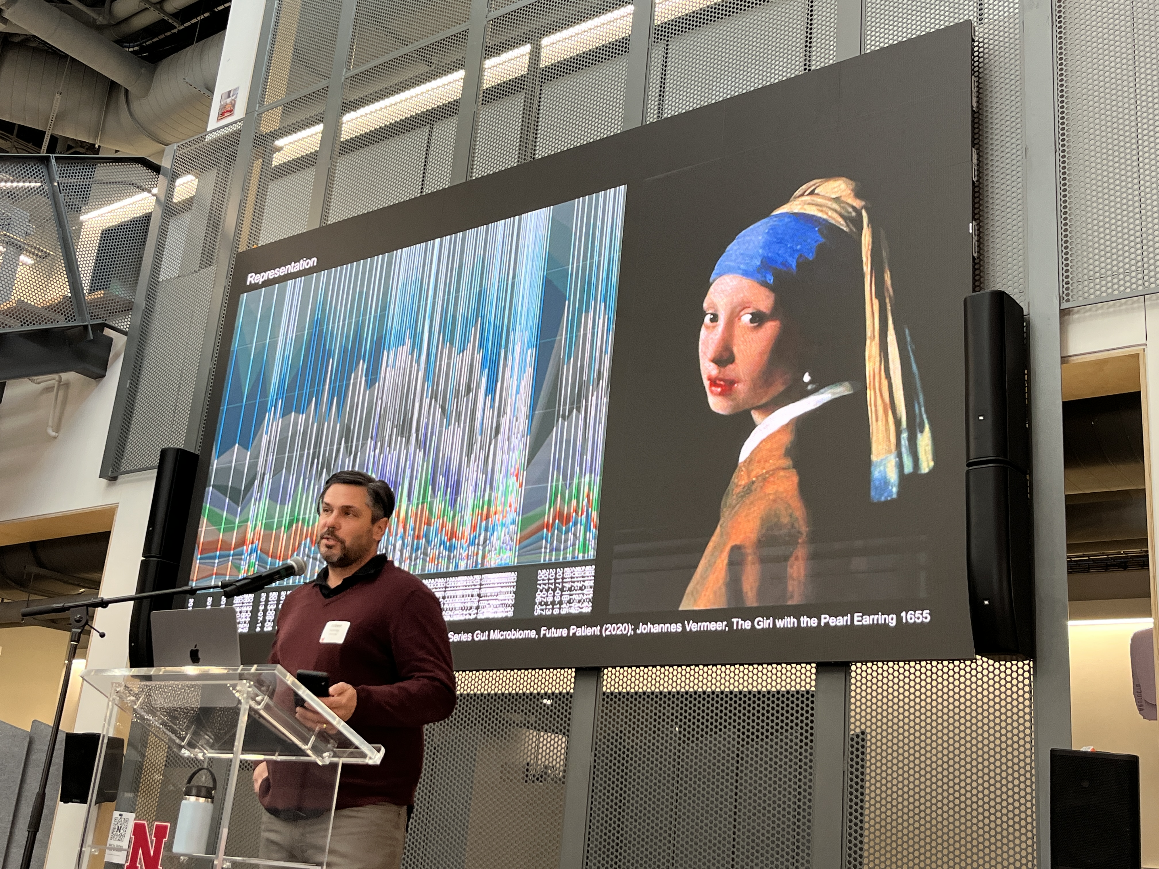 photo of Prof. Twomey on stage with slide behind showing data and painting