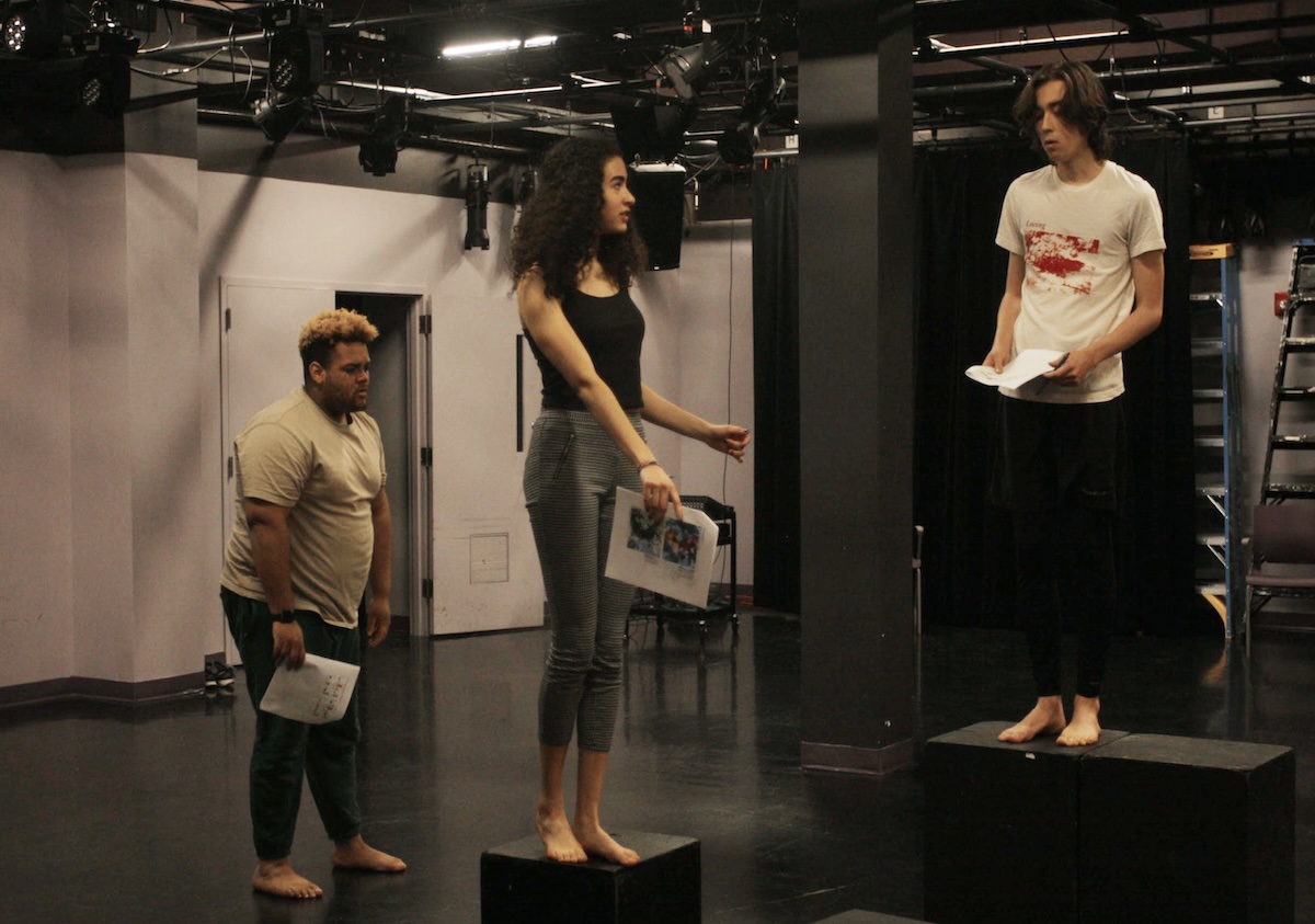 photo of three students standing in an open theatre space with data handouts in their hands