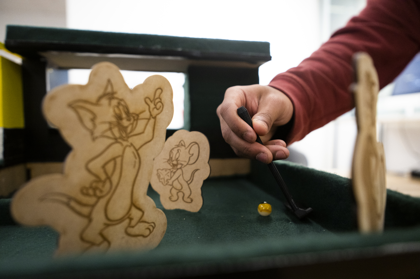 close-up of person's hand using hand-held putter to tap a marble around laser-cut certical obstacles of Tom and Jerry